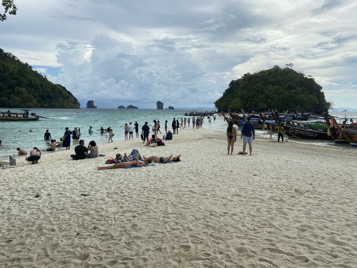 A lively beach scene with people relaxing on the sand and enjoying the clear water, surrounded by lush green islands
